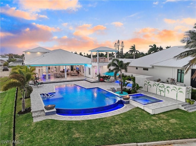 pool at dusk with a gazebo, an in ground hot tub, a lawn, and a patio