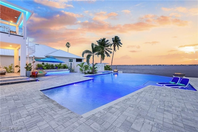 pool at dusk with a water view and a patio area