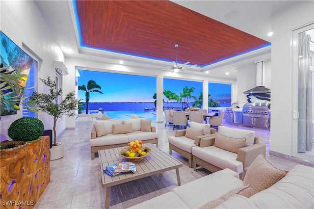 living room with a tray ceiling, ceiling fan, a water view, and wood ceiling