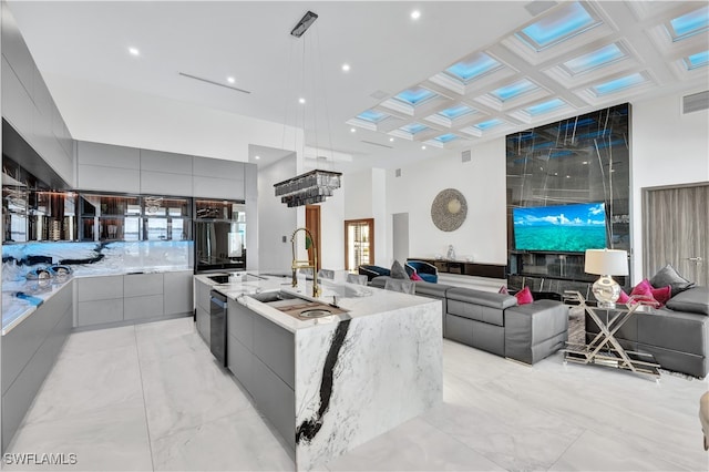 kitchen featuring pendant lighting, a large island with sink, coffered ceiling, stainless steel dishwasher, and gray cabinets