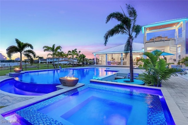 pool at dusk featuring an in ground hot tub and a patio