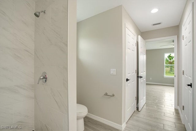 bathroom featuring a tile shower, ceiling fan, hardwood / wood-style floors, and toilet