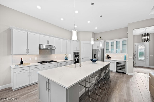 kitchen featuring appliances with stainless steel finishes, white cabinetry, wine cooler, and an island with sink