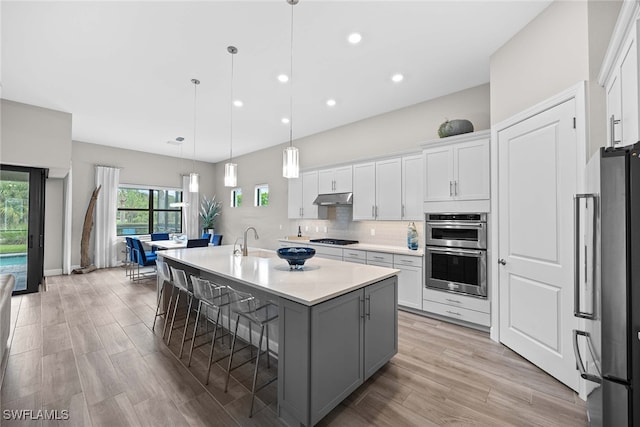 kitchen with a kitchen bar, appliances with stainless steel finishes, a center island with sink, white cabinetry, and hanging light fixtures