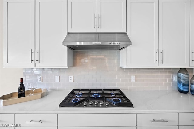 kitchen featuring light stone countertops, backsplash, extractor fan, white cabinets, and stainless steel gas stovetop