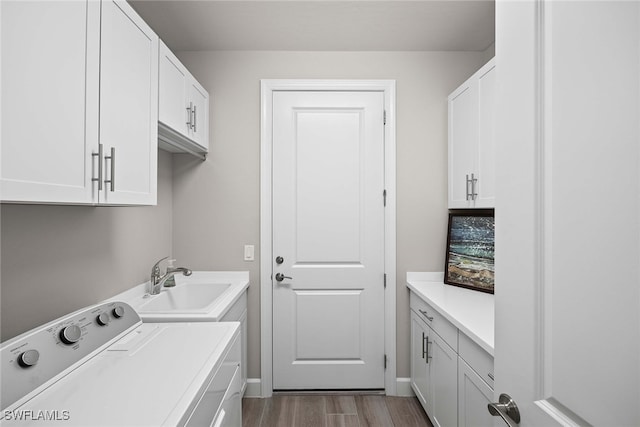 clothes washing area with cabinets, hardwood / wood-style floors, washer and clothes dryer, and sink