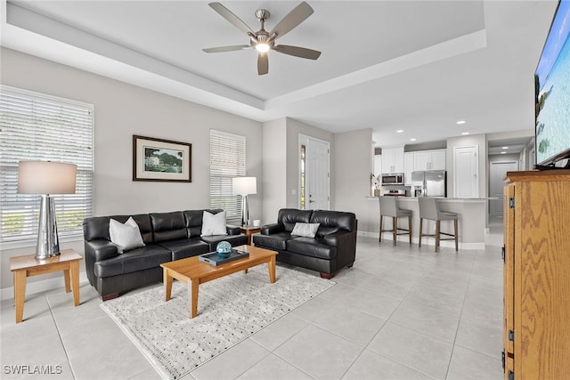 tiled living room featuring a raised ceiling and ceiling fan