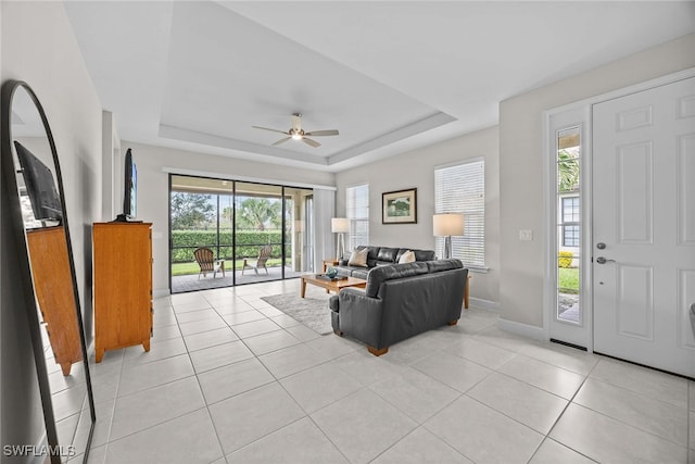 living room with a raised ceiling, ceiling fan, and light tile patterned floors