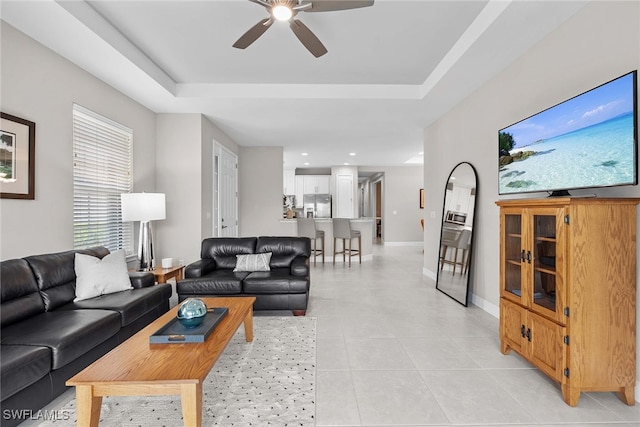 tiled living room featuring a raised ceiling and ceiling fan