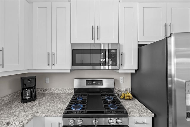 kitchen with white cabinets, appliances with stainless steel finishes, and light stone countertops