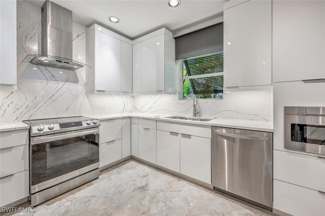 kitchen featuring light stone countertops, white cabinetry, sink, stainless steel appliances, and wall chimney range hood