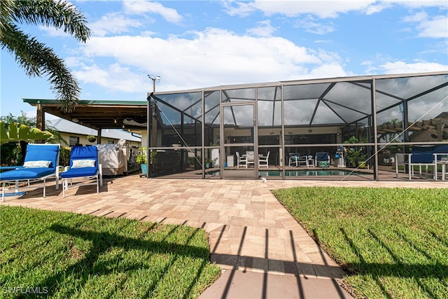 rear view of house featuring a lawn, glass enclosure, and a patio