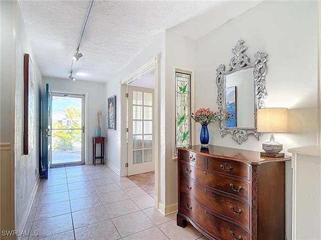 doorway featuring rail lighting, light tile patterned floors, and a textured ceiling