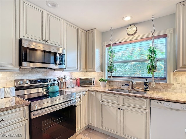 kitchen with sink, decorative backsplash, light stone countertops, light tile patterned floors, and stainless steel appliances