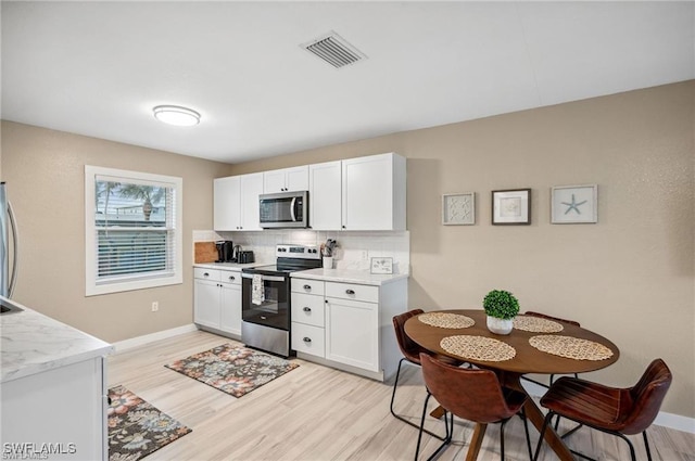 113/115 Bahia Viaduct, Fort Myers Beach, FL 33931 - kitchen with appliances with stainless steel finishes, tasteful backsplash, light wood finished floors, white cabinets, and light countertops