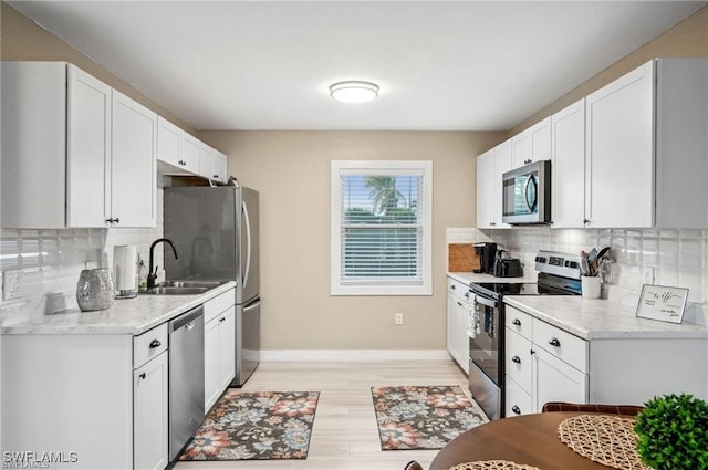 kitchen with appliances with stainless steel finishes, white cabinets, a sink, and decorative backsplash