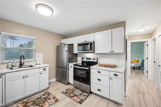 kitchen with white cabinets, stainless steel appliances, a sink, and light countertops