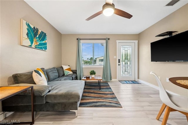 living area featuring a ceiling fan, baseboards, visible vents, and light wood finished floors