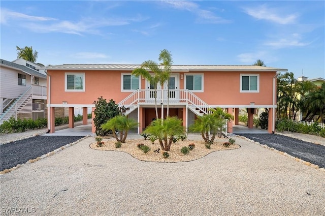 beach home featuring metal roof, driveway, stairway, a carport, and a standing seam roof