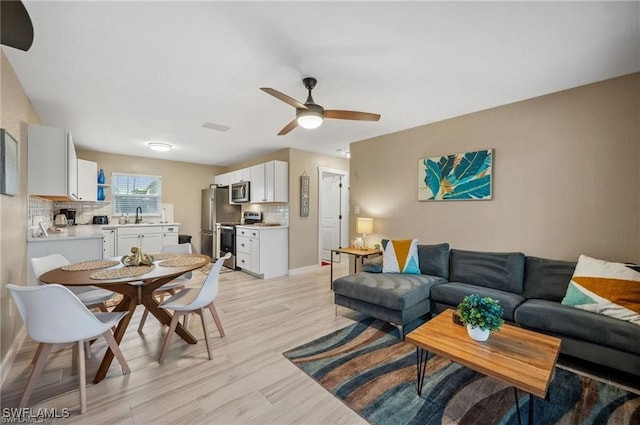 living room featuring light wood-style flooring, baseboards, and a ceiling fan