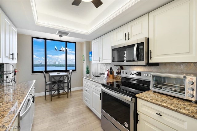 kitchen with white cabinets, a tray ceiling, decorative light fixtures, light stone counters, and stainless steel appliances