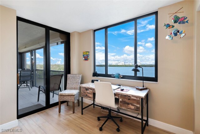 office space featuring a wall of windows, plenty of natural light, a water view, and light wood-type flooring