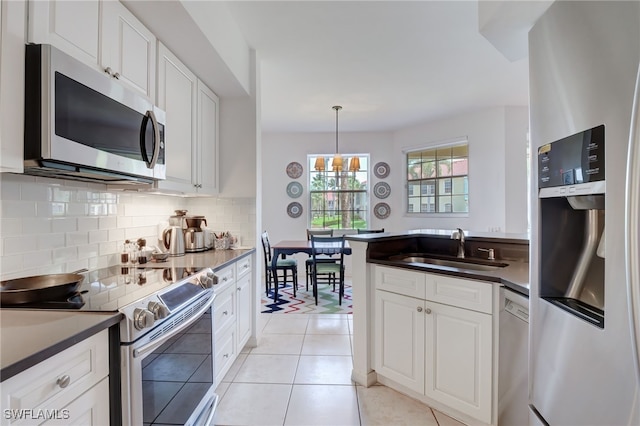 kitchen with sink, hanging light fixtures, light tile patterned flooring, white cabinets, and appliances with stainless steel finishes