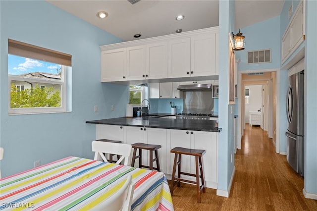 kitchen with dark hardwood / wood-style flooring, ventilation hood, white cabinetry, and stainless steel refrigerator