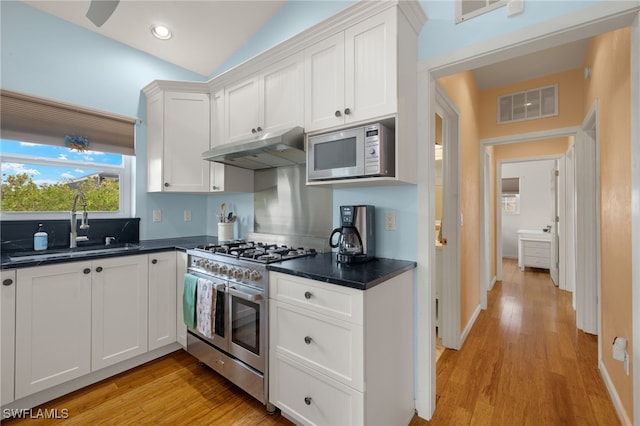 kitchen with lofted ceiling, white cabinets, sink, light wood-type flooring, and appliances with stainless steel finishes