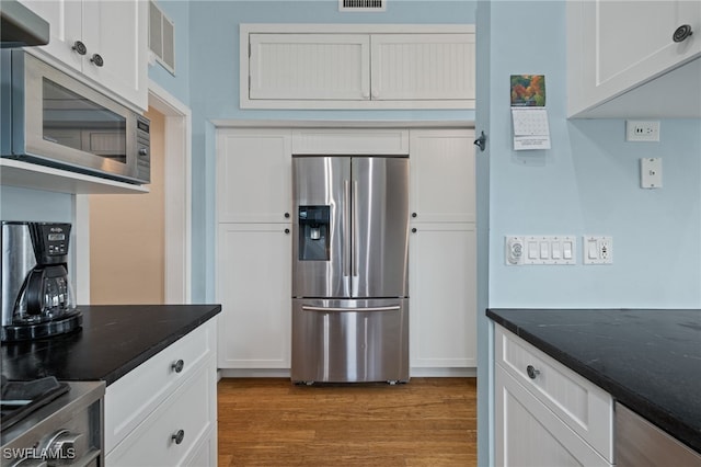 kitchen featuring appliances with stainless steel finishes, light wood-type flooring, exhaust hood, dark stone countertops, and white cabinets