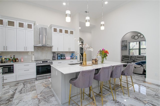 kitchen with white cabinets, a center island with sink, wall chimney range hood, electric range, and decorative light fixtures