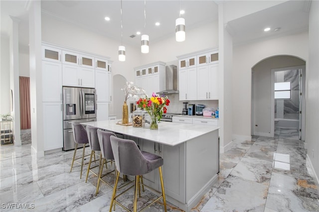 kitchen with pendant lighting, a center island with sink, wall chimney range hood, appliances with stainless steel finishes, and white cabinetry