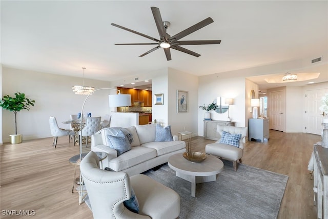 living room featuring ceiling fan with notable chandelier and light wood-type flooring