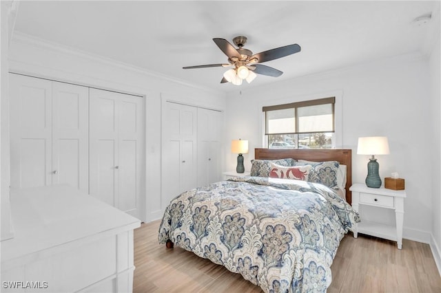 bedroom with two closets, light hardwood / wood-style flooring, ceiling fan, and crown molding