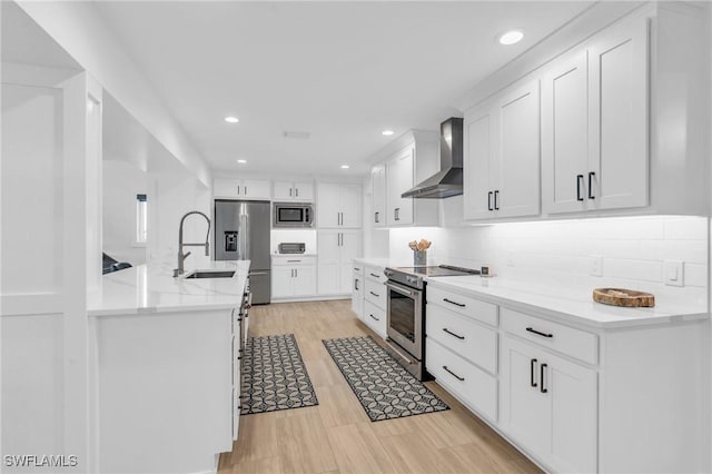 kitchen with white cabinets, light hardwood / wood-style floors, wall chimney range hood, and appliances with stainless steel finishes