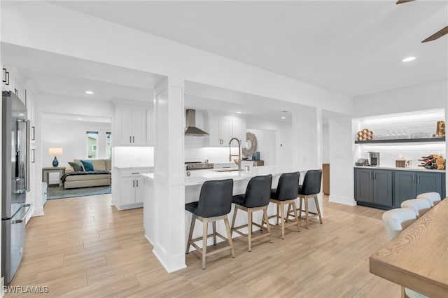 kitchen featuring white cabinets, wall chimney exhaust hood, stainless steel fridge, and light hardwood / wood-style flooring