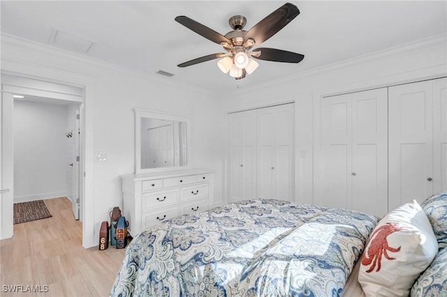 bedroom featuring ceiling fan, multiple closets, crown molding, and light hardwood / wood-style flooring