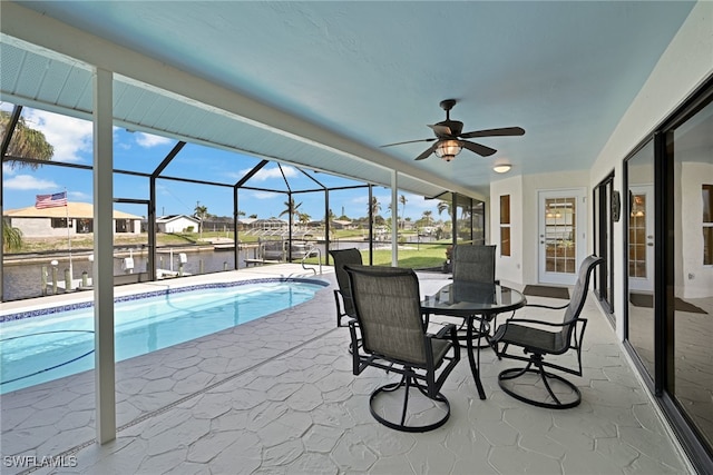 view of pool with glass enclosure, ceiling fan, a water view, and a patio