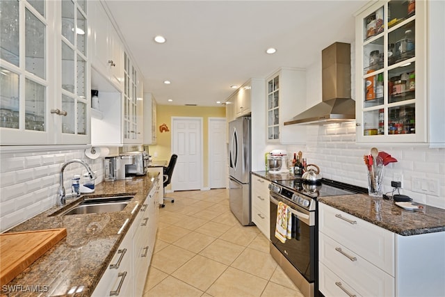 kitchen featuring appliances with stainless steel finishes, dark stone counters, wall chimney exhaust hood, sink, and white cabinets