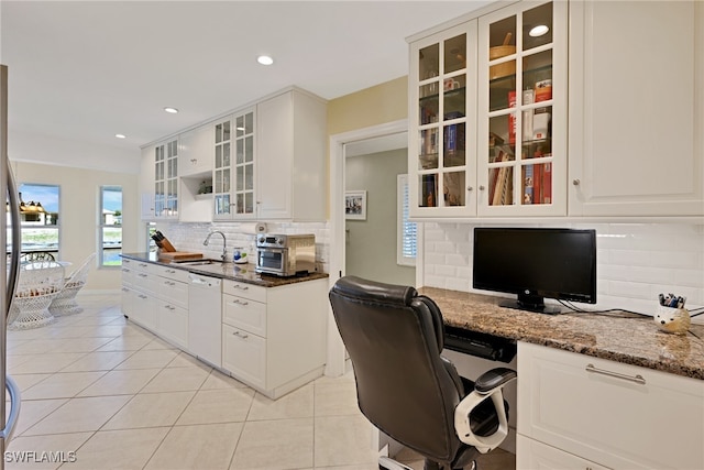 kitchen with white cabinets, built in desk, tasteful backsplash, and dark stone countertops