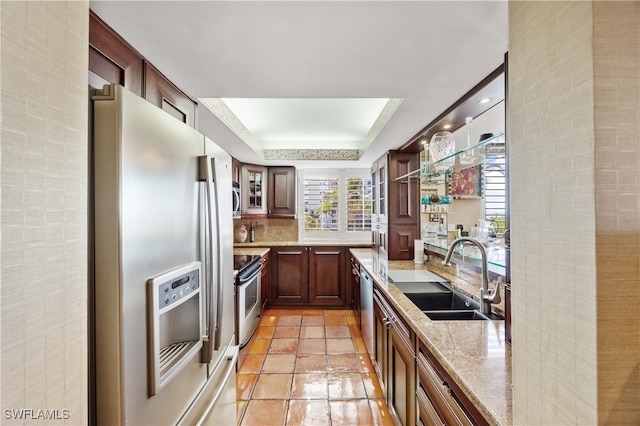 kitchen featuring light stone countertops, appliances with stainless steel finishes, a tray ceiling, sink, and light tile patterned flooring