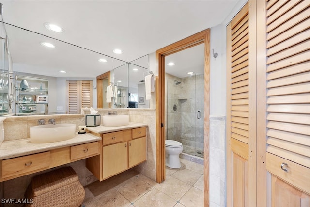 bathroom featuring vanity, a shower with door, tile patterned floors, toilet, and tile walls