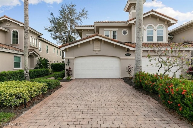 mediterranean / spanish-style home with stucco siding, a tiled roof, decorative driveway, and a garage