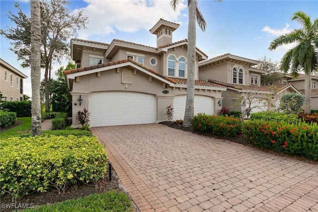 mediterranean / spanish-style home featuring stucco siding, an attached garage, a tile roof, and decorative driveway