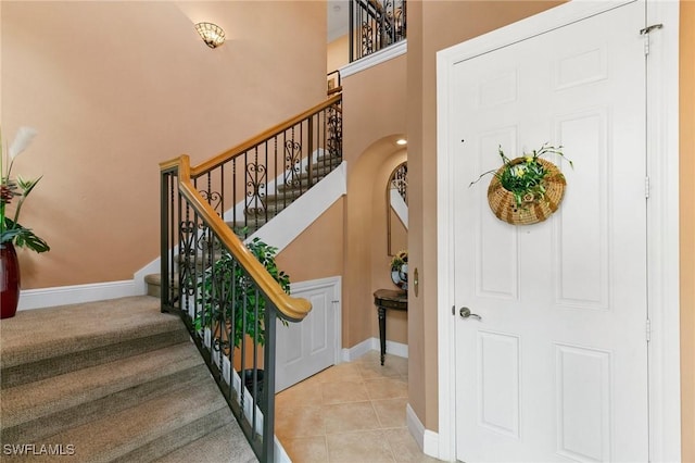 stairs with tile patterned floors, baseboards, and arched walkways