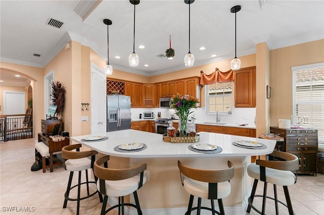 kitchen with a sink, backsplash, stainless steel appliances, brown cabinetry, and light countertops