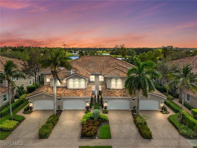 mediterranean / spanish home featuring stucco siding, decorative driveway, a garage, and a tile roof