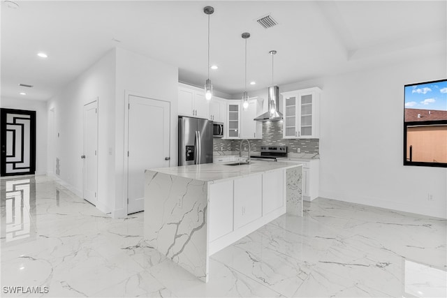 kitchen with a kitchen island with sink, white cabinets, wall chimney range hood, light stone counters, and stainless steel appliances