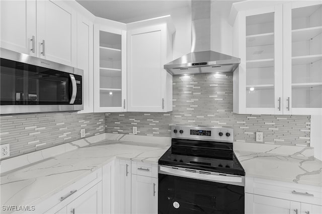 kitchen featuring light stone countertops, white cabinets, stainless steel appliances, and wall chimney range hood