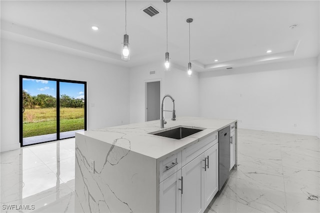 kitchen with light stone countertops, a tray ceiling, sink, pendant lighting, and a center island with sink